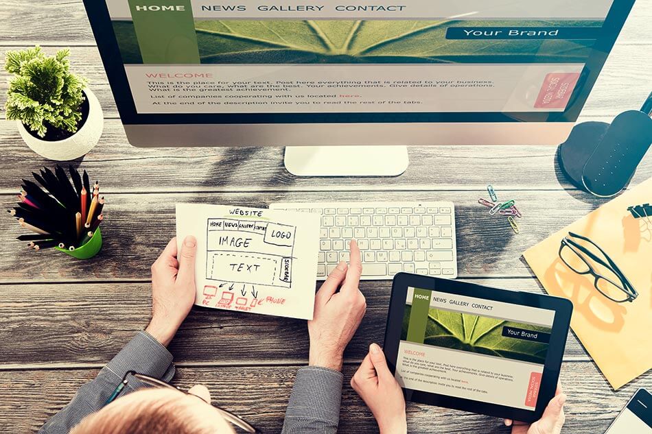 Two people reviewing wireframes on paper and a webpage on a tablet and a desktop computer